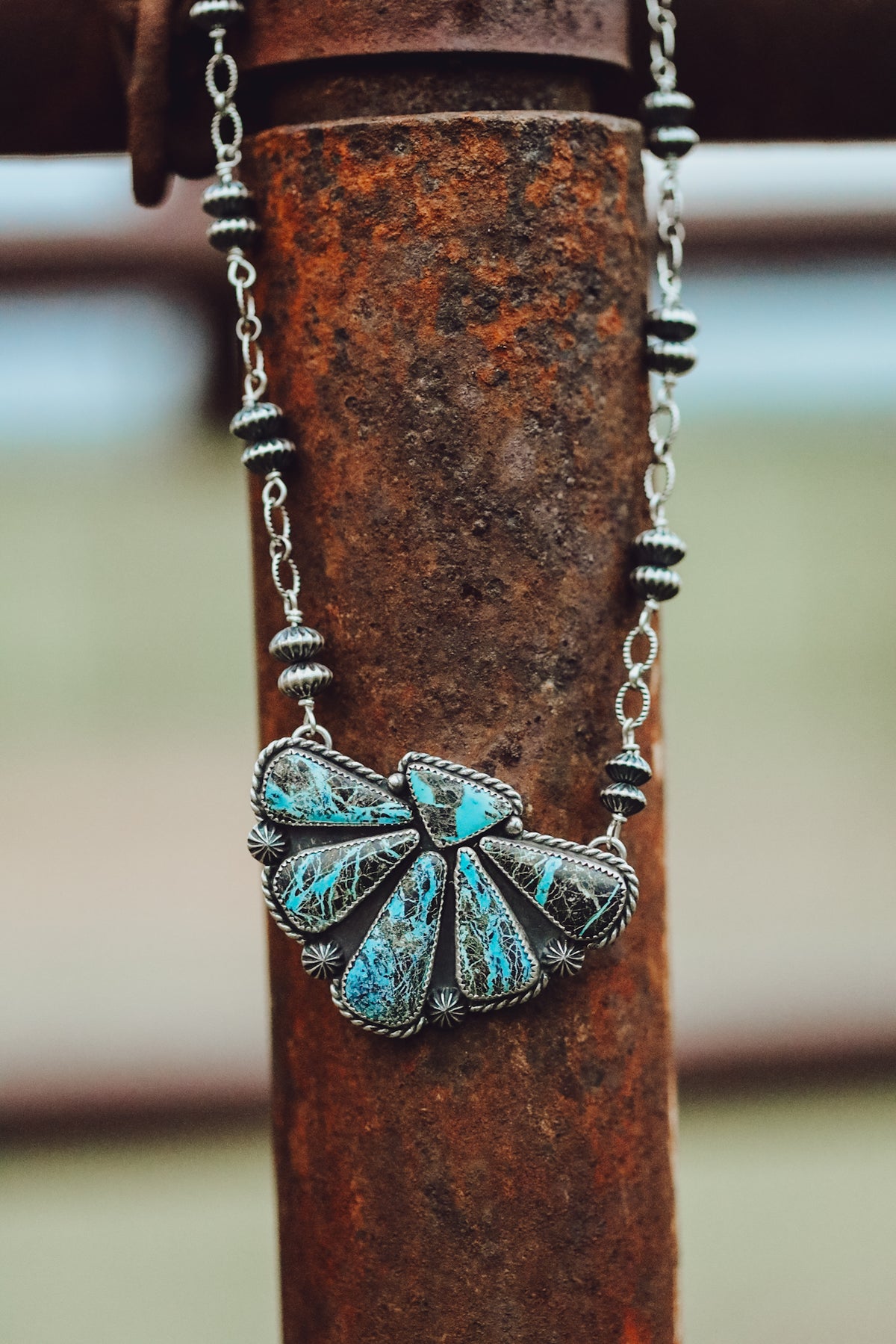 A silver necklace with a half cluster turquoise pendant, displayed against a rustic metal background.